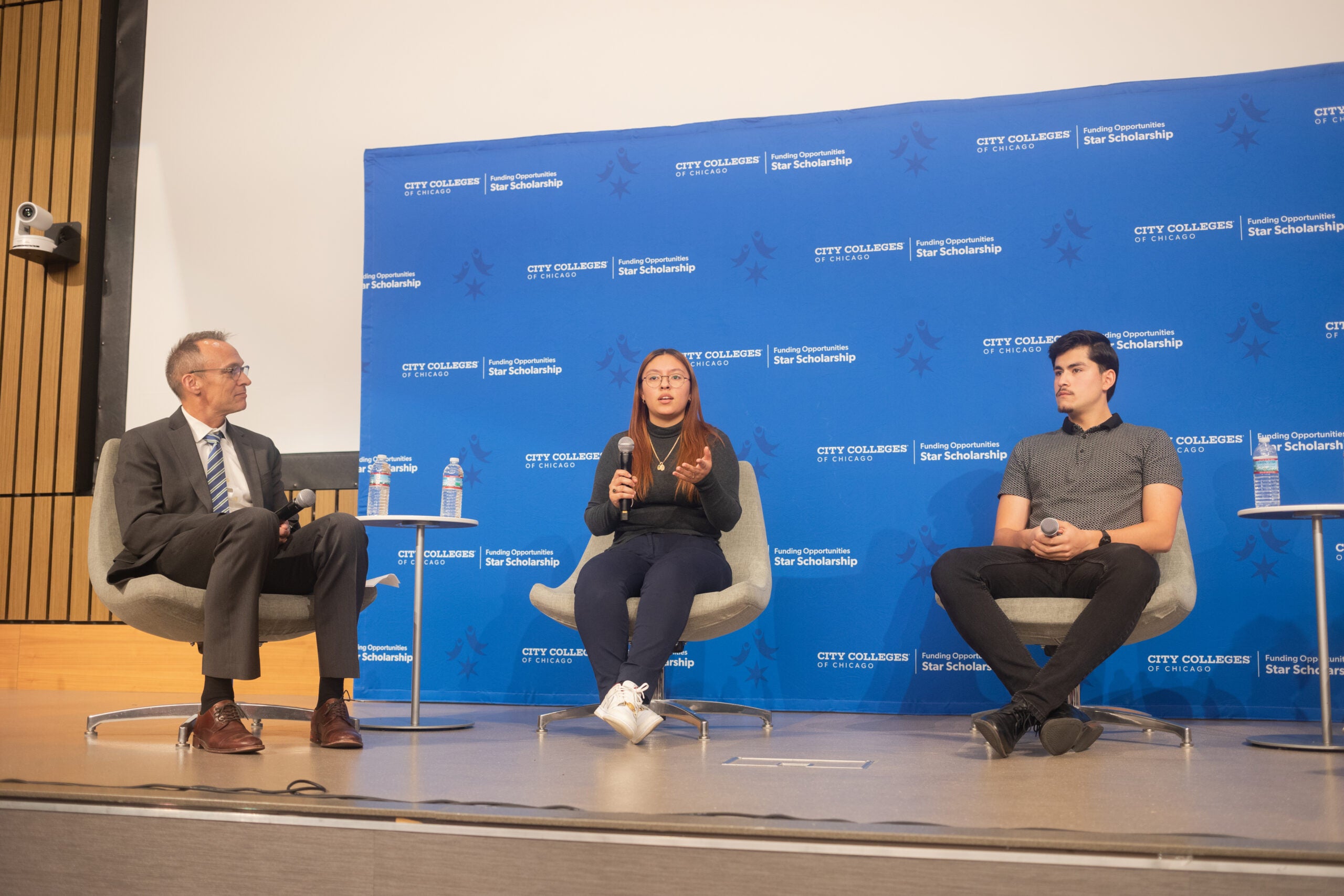 Four people sit on stage in front of a blue background and speak on a panel.