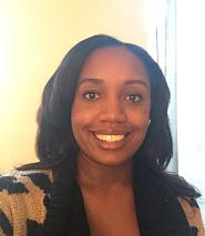 A woman smiles head on to the camera. She has shoulder length dark hair and is posed in front of a white wall.