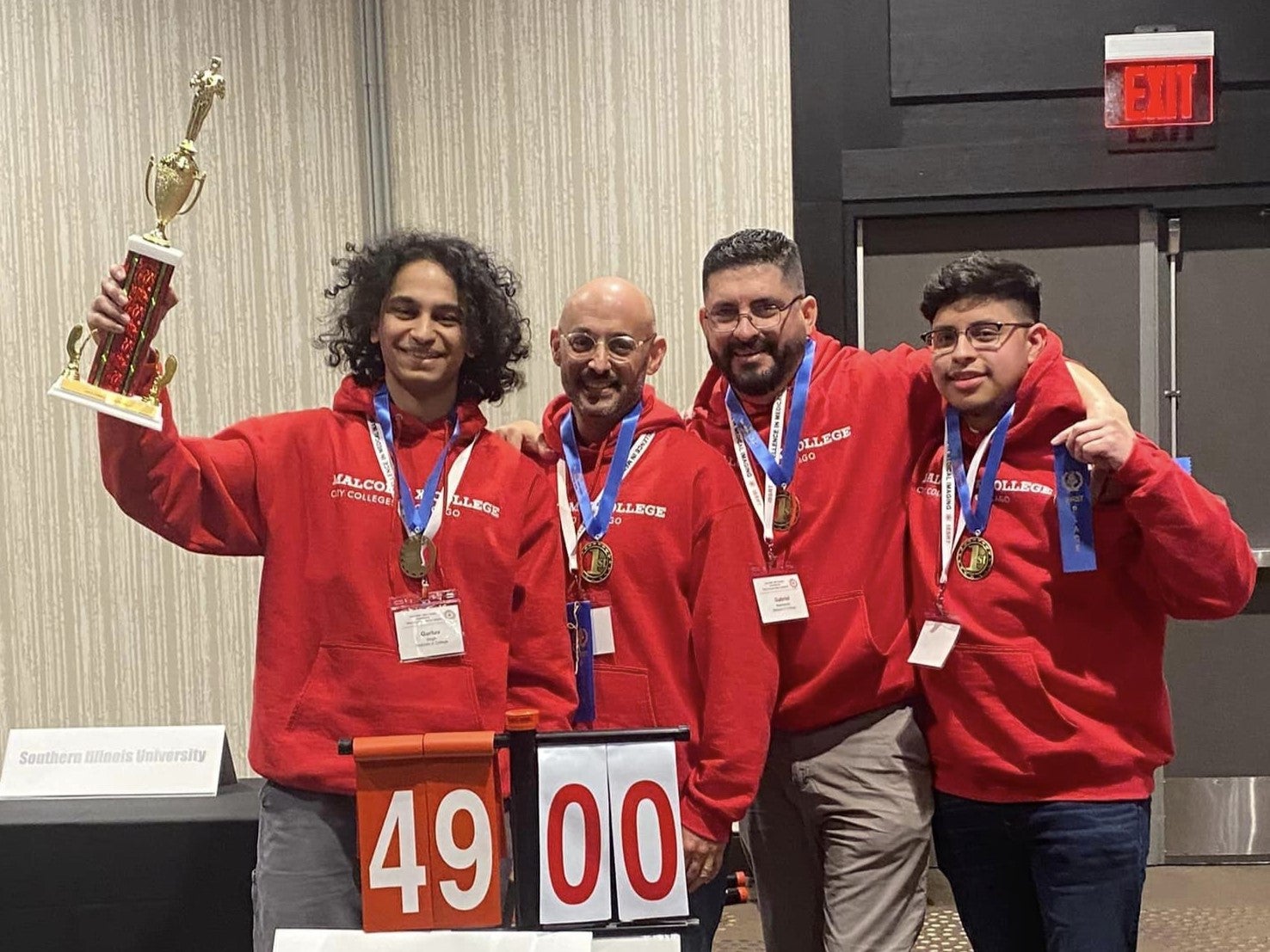 Four students pose for a photo with medals around their necks. One is holding a trophy.